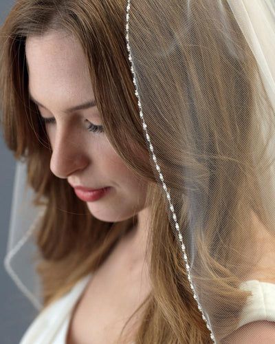 a woman wearing a wedding veil with beads on it's head and her hair in the wind