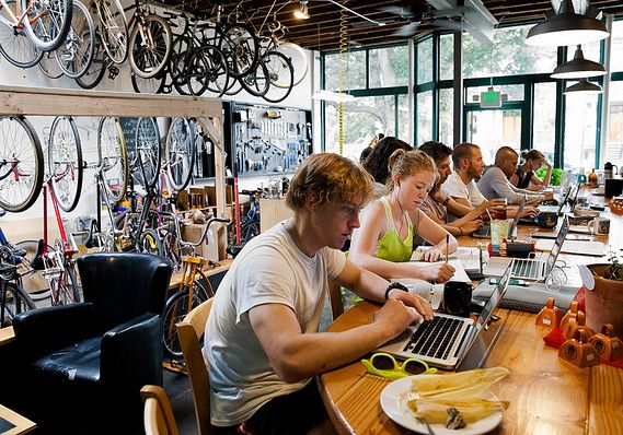 a group of people sitting at a table working on laptops in a bike shop