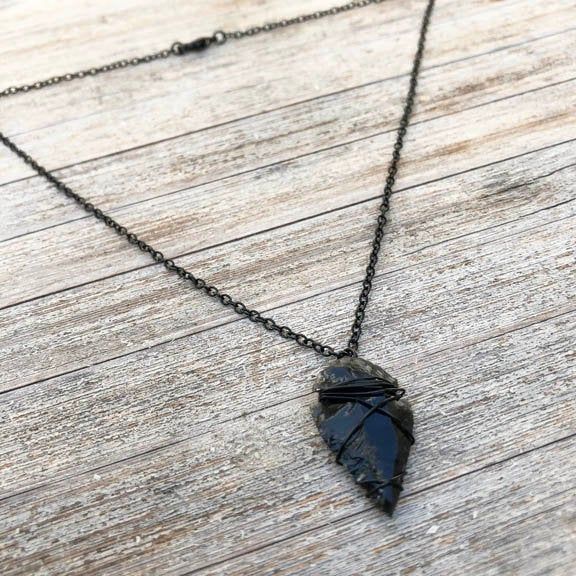 "Attract success and abundance in this minimalist wire-wrapped, arrowhead necklace. Makes a perfect Father's Day or graduation gift. It can be worn alone or layered for a modern boho look. Arrowhead is approximately 1\" (one inch) in length. Arrowheads are hand-knapped and vary slightly in size, shape and color. Each will have sight variations in texture and wire wrapping to accommodate individual characteristics. The chain is a nickel-free base metal, coated in black. This design is handmade by Handmade Sterling Silver Arrowhead Necklace, Adjustable Hand Forged Black Jewelry, Black Wire Wrapped Pendant Jewelry, Hand Forged Black Jewelry As Gift, Black Hand Forged Jewelry For Gift, Unique Hand Forged Black Necklace, Hand Forged Black Jewelry Gift, Arrowhead Wire Wrapped Necklaces For Gifts, Adjustable Wire Wrapped Arrowhead Necklace