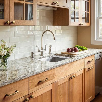 a kitchen with wooden cabinets and marble counter tops, along with white flowers on the window sill