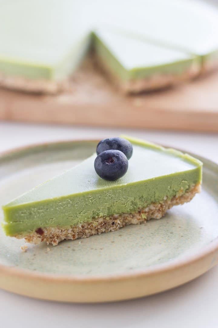 a slice of raw matcha cheesecake on a plate with blueberries next to it