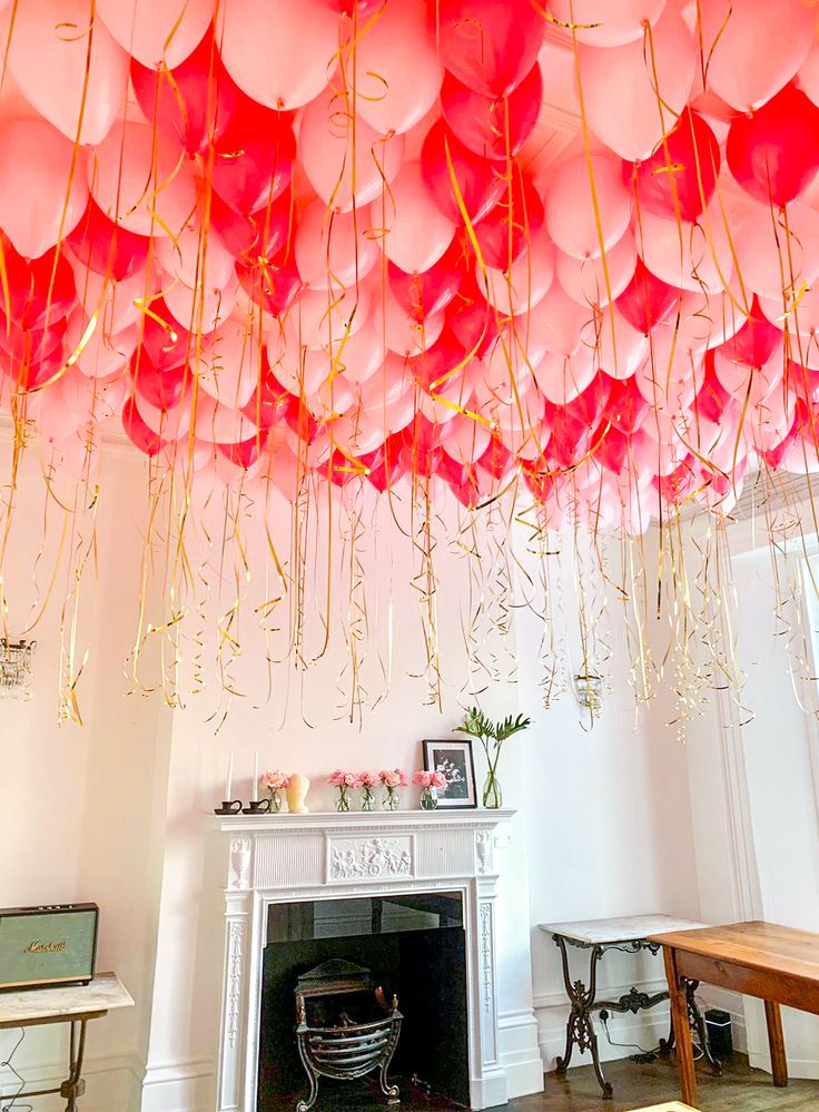 pink and red balloons are hanging from the ceiling above a fireplace in a living room