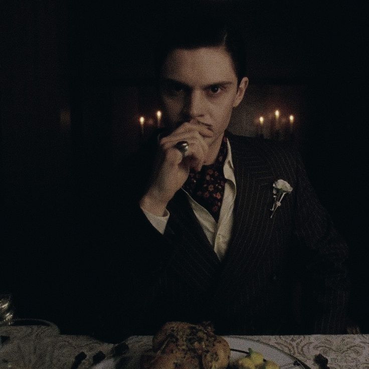 a man sitting at a table with food in front of him and lit candles behind him