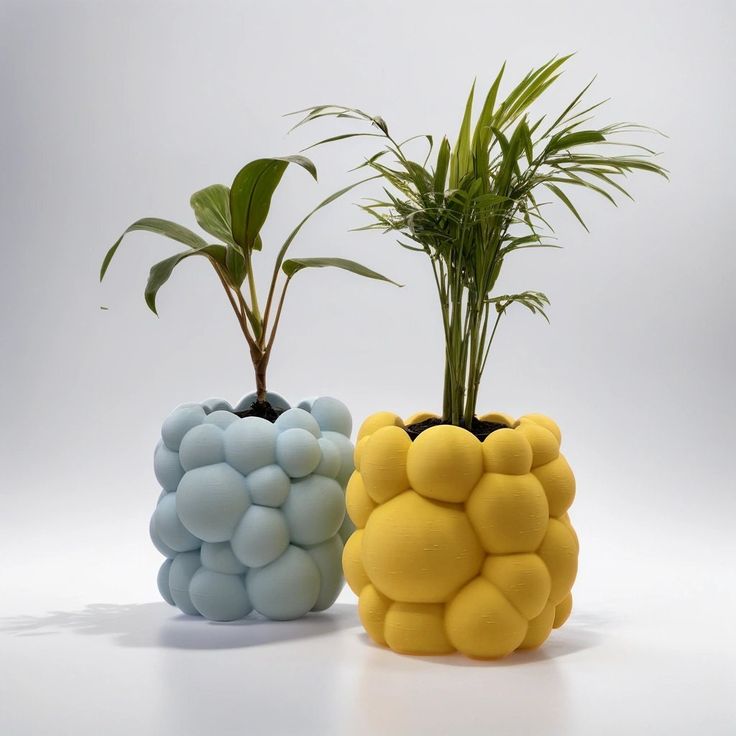 two planters with plants in them sitting next to each other on a white surface