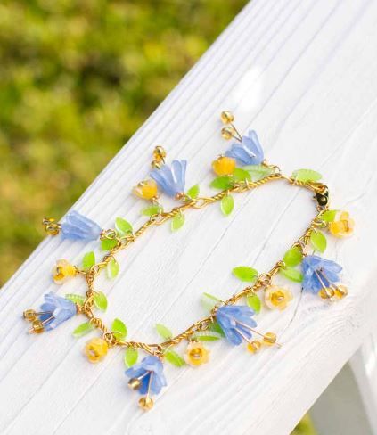 a bracelet with blue flowers and green leaves on it sitting on a white wooden bench