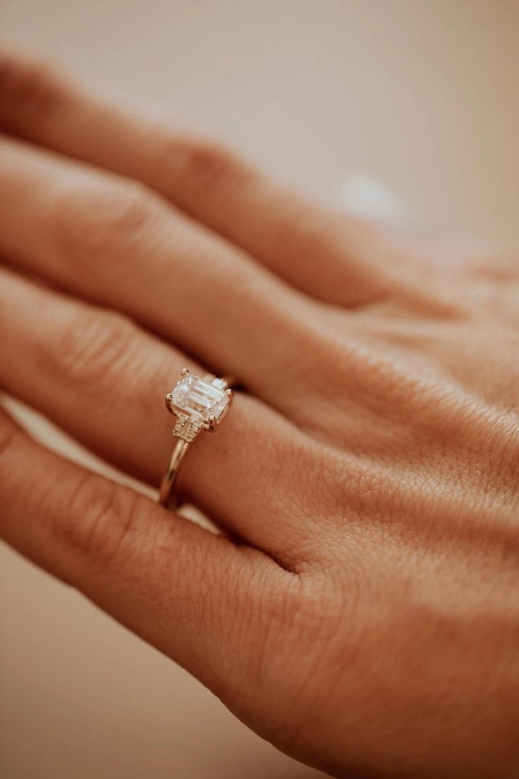 a woman's hand holding an engagement ring with a diamond in the middle, on top of her finger