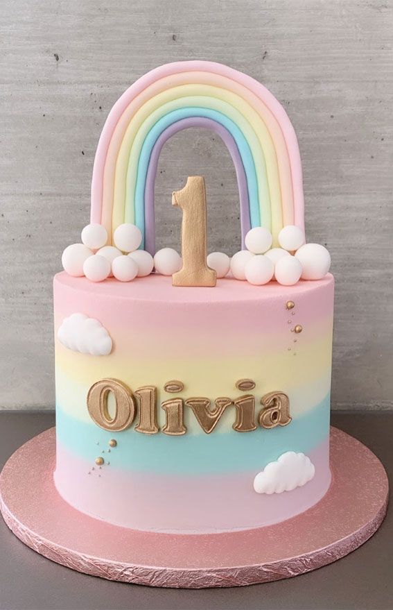 a pink and blue cake with a number one on the top is decorated with rainbows