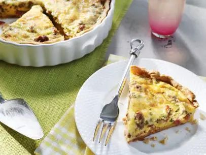 a slice of quiche on a plate with a fork and glass of pink juice