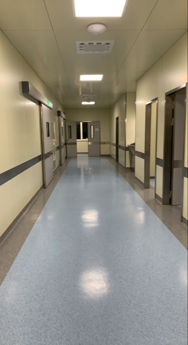 an empty hospital hallway with blue floors and doors on either side of the door is a light fixture