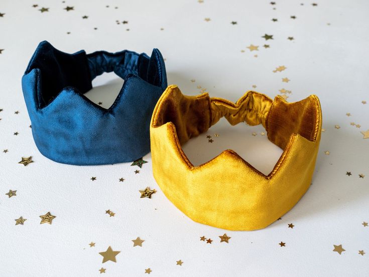 two little crowns sitting on top of a white table next to each other with gold stars around them