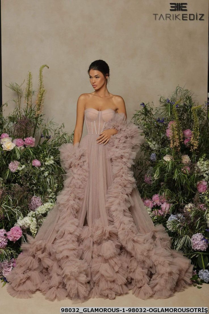 a woman standing in front of flowers wearing a dress with ruffles on it