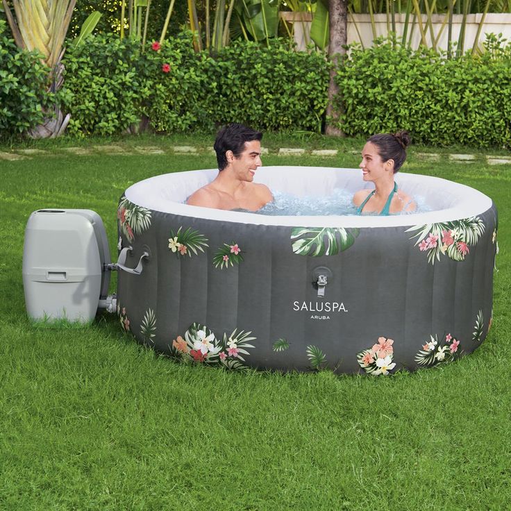 two people sitting in an inflatable hot tub on the grass near some bushes