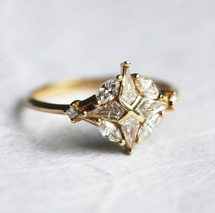 a three stone diamond ring sitting on top of a white surface with gold trimmings