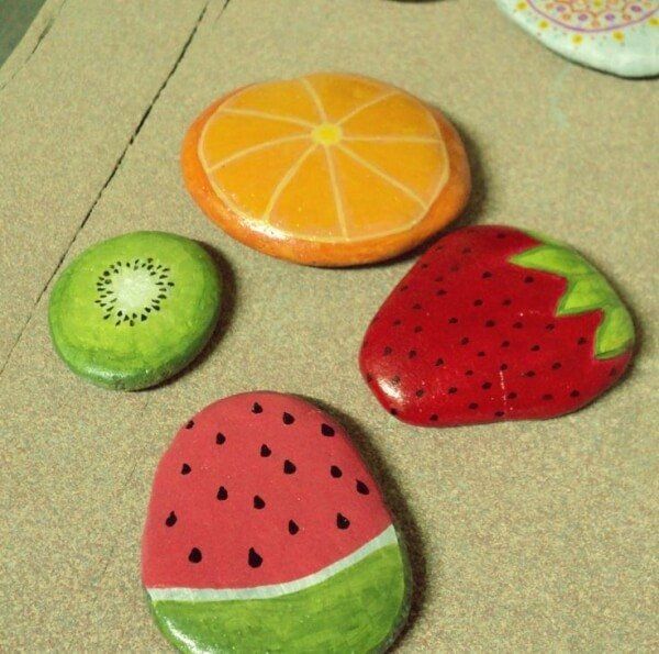 four painted rocks with fruit on them sitting on the floor next to each other,