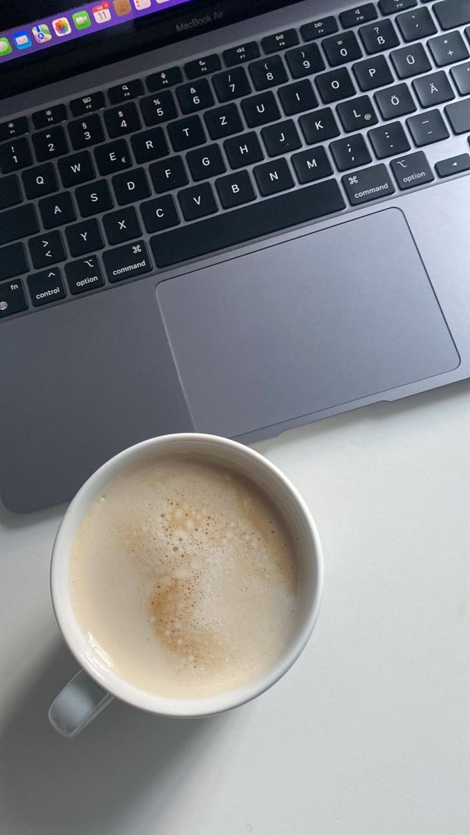 a cup of coffee sitting next to an open laptop computer on a white table top