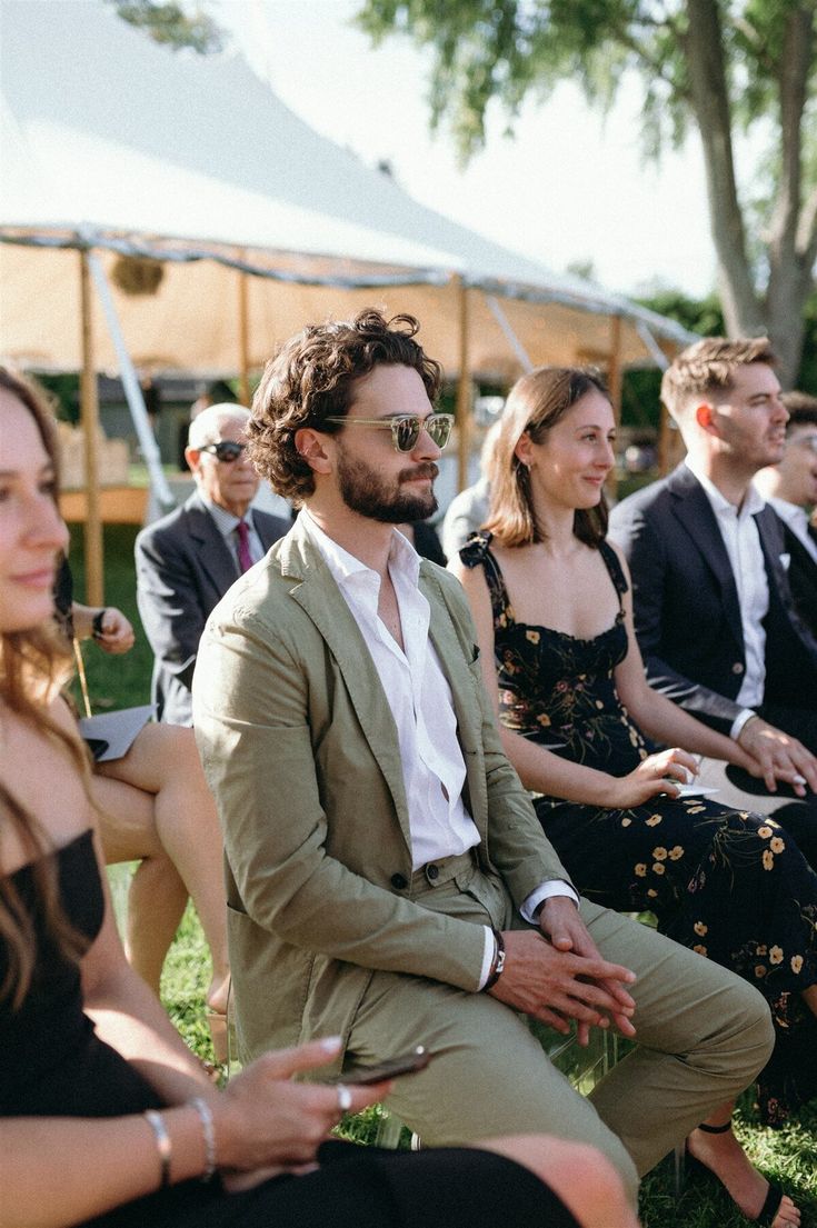 a group of people sitting next to each other on top of a grass covered field