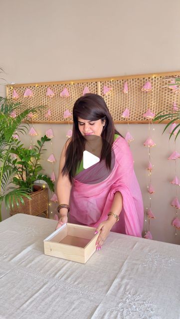 a woman in a pink sari is opening a box on a table with flowers