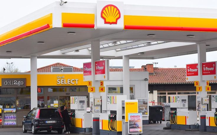 a shell gas station with two cars parked at it's pumps and people standing around