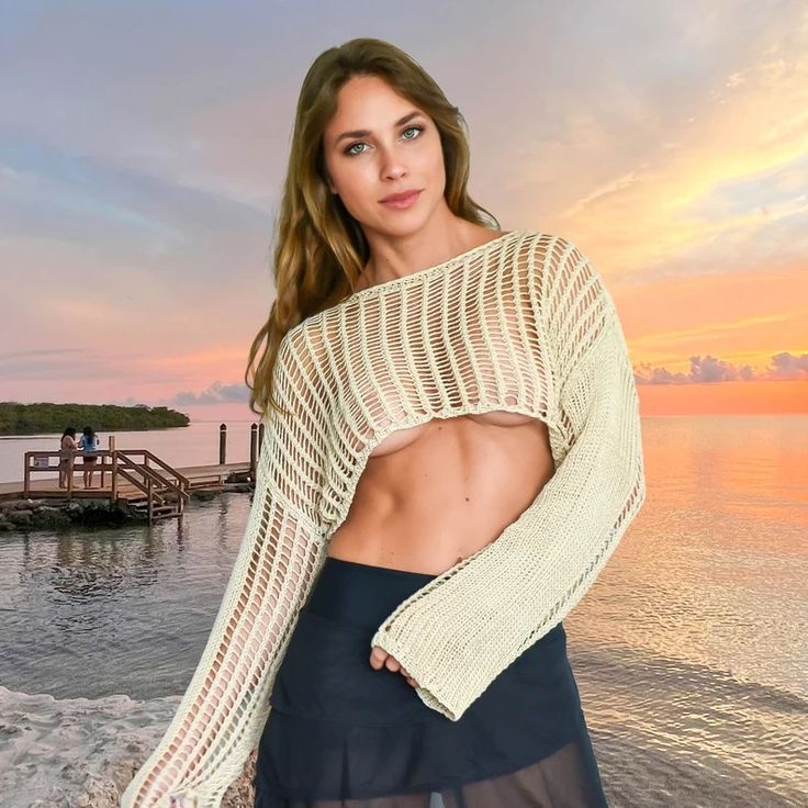 a woman standing on top of a beach next to the ocean wearing a white sweater