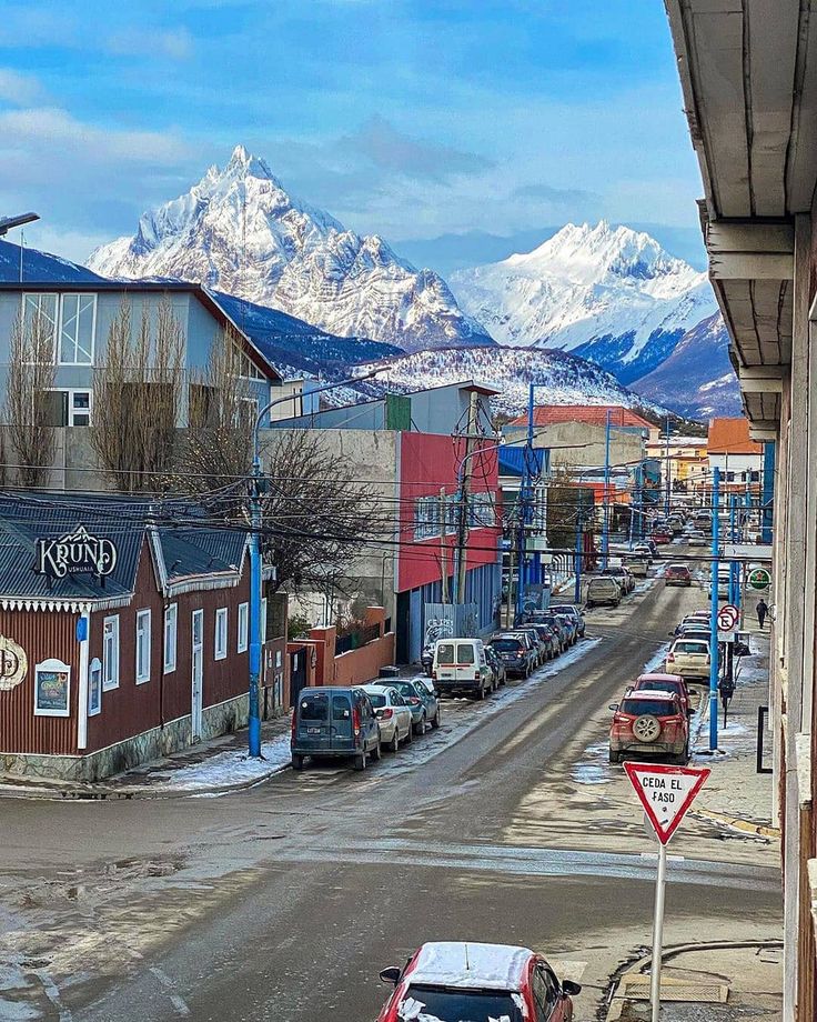 cars parked on the side of a road in front of buildings with mountains in the background