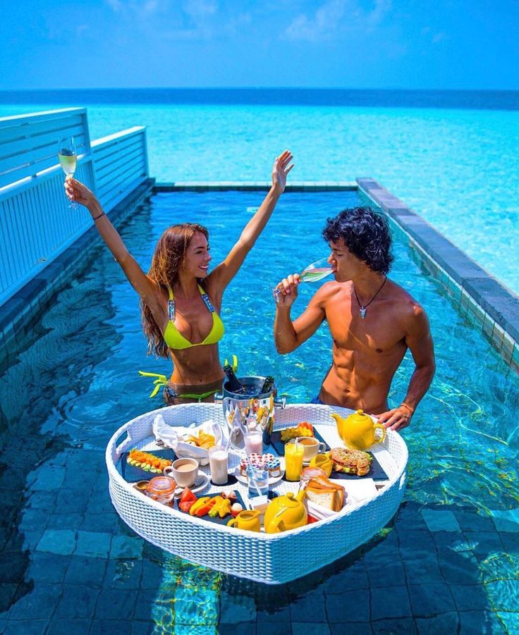 a man and woman in bikinis standing next to a table with food on it