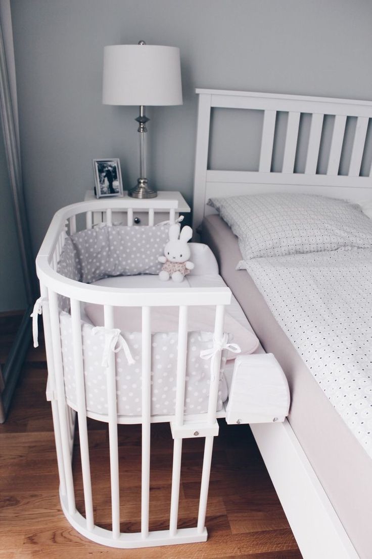 a baby crib next to a bed with a lamp on the nightstand and pictures on the wall