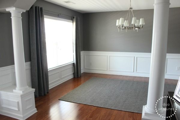 a living room with hard wood floors and gray walls, white trim around the windows