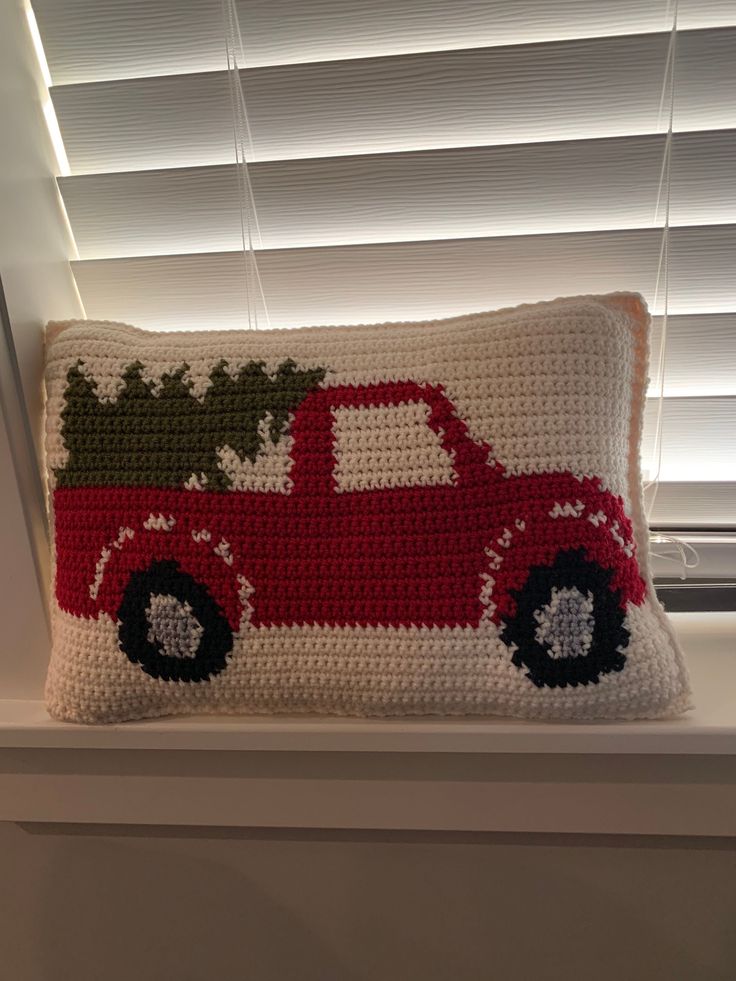 a crocheted pillow with a red truck carrying a christmas tree on it's back