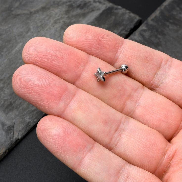 a tiny silver star shaped nose piercing on someone's palm with a black background