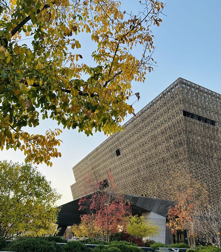 a large building with a triangular roof next to trees and bushes in front of it