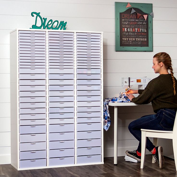 a woman sitting at a table in front of a large stack of white filing cabinets