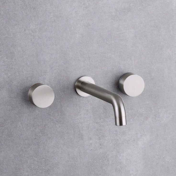 two chrome faucets on a gray wall with white knobs and round handles