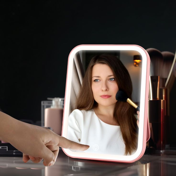 a woman's hand is holding a makeup brush in front of a mirror with the reflection of her face