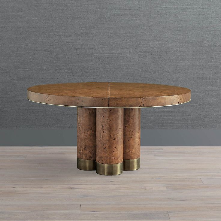 a round wooden table with two brass legs on a wood floor in front of a gray wall