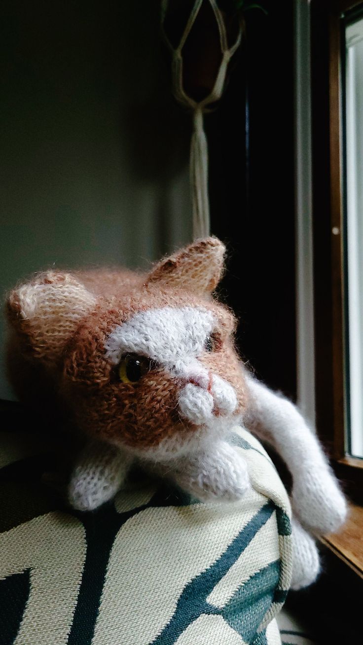 an orange and white stuffed animal sitting on top of a pillow next to a window