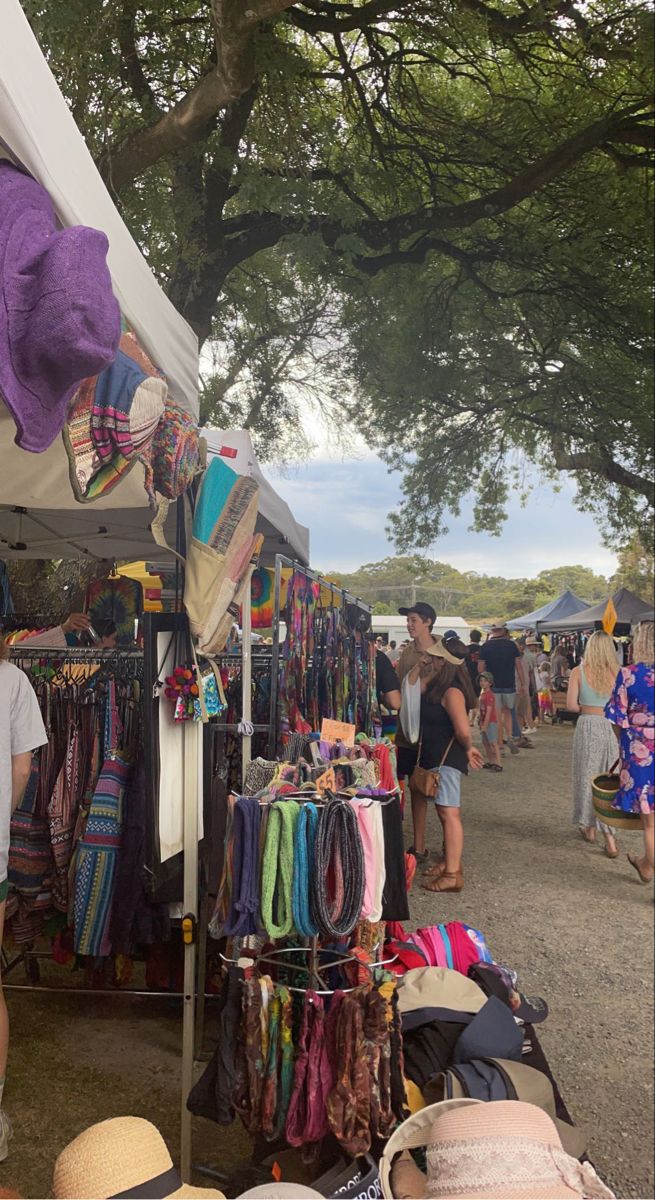 people shopping at an outdoor market with hats and scarves hanging from the tents on display