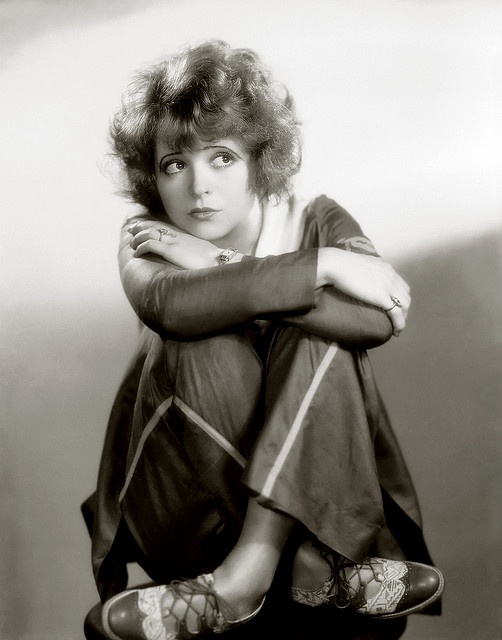 black and white photograph of a woman sitting on a stool with her legs crossed over her knees