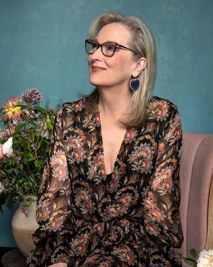 a woman with glasses sitting on a chair in front of a flower pot and vase