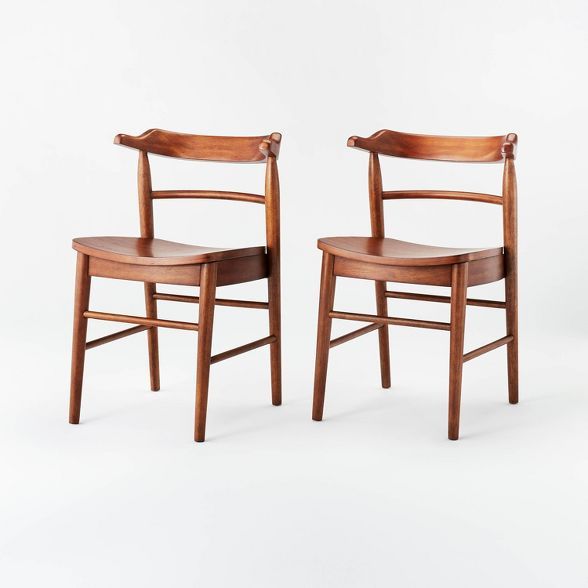 two wooden chairs sitting next to each other on a white surface with one chair facing the other