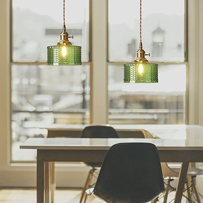 two green glass pendant lights hanging over a dining room table with chairs in front of large windows