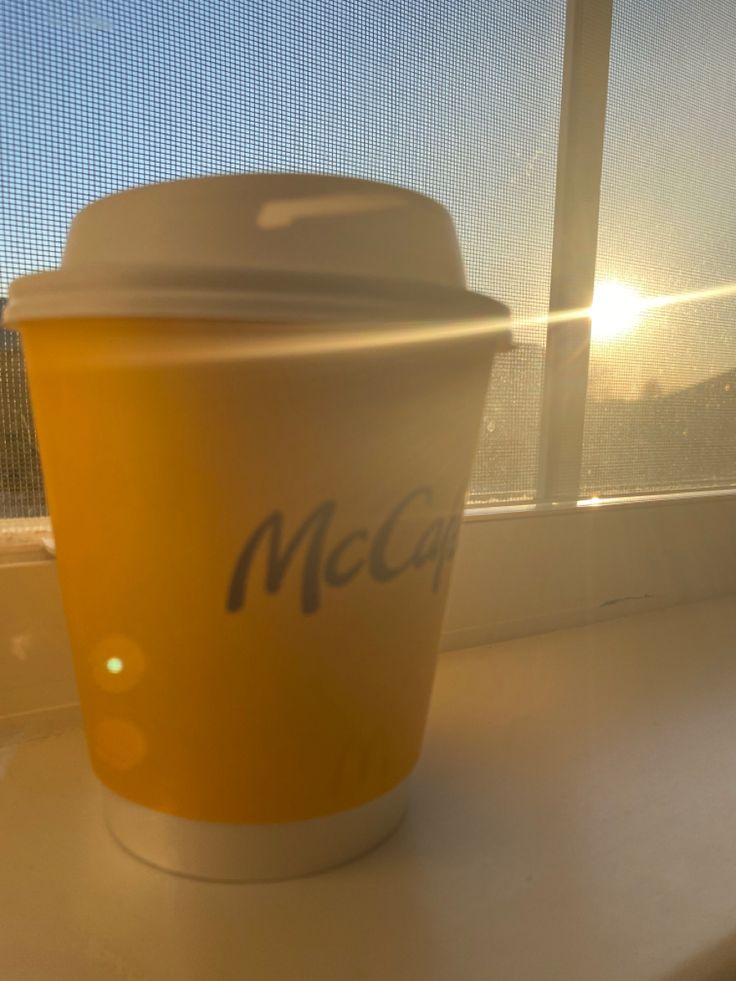 a yellow cup sitting on top of a window sill next to a sunlit window