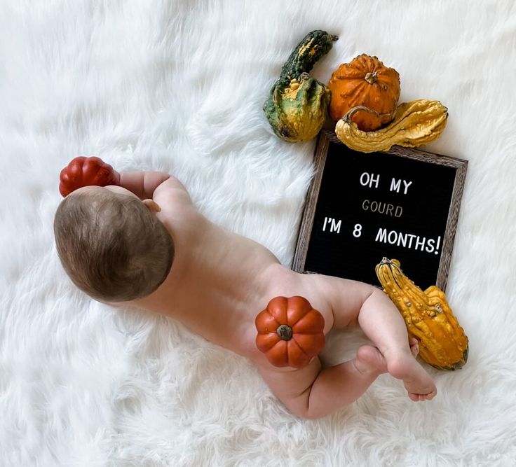 a baby laying on top of a white blanket next to pumpkins and gourds