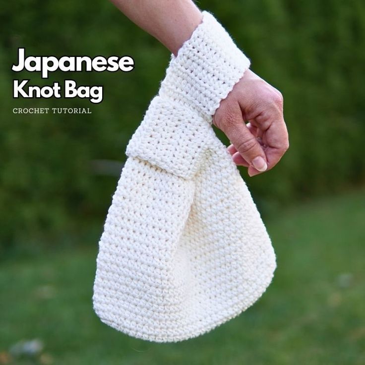 a hand holding a white crochet bag in front of green grass and bushes