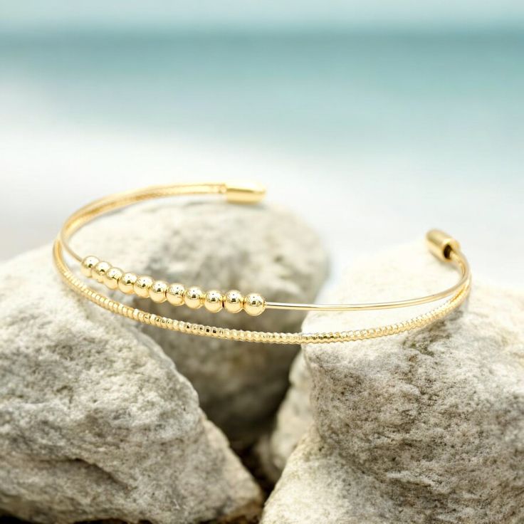 This beautiful double-strand bracelet is lightweight, bendable, and shiny, making it comfortable to wear. It is gold-plated, ensuring it maintains its stunning shine, especially when kept away from water. This bracelet is perfect for complementing our tile bracelets, but it also makes a great statement piece on its own. Gold Stackable Double Band Bracelets, Stackable Double Band Gold Bracelets, Elegant Double Band Gold Cuff Bracelet, Elegant Gold Double Band Cuff Bracelet, Gold Adjustable Double Strand Beaded Bracelets, Gold Double Band Bracelets, Gold Double Band Bangle As A Gift, Gold Adjustable Double Band Bracelet, Gold Double Band Adjustable Bracelets