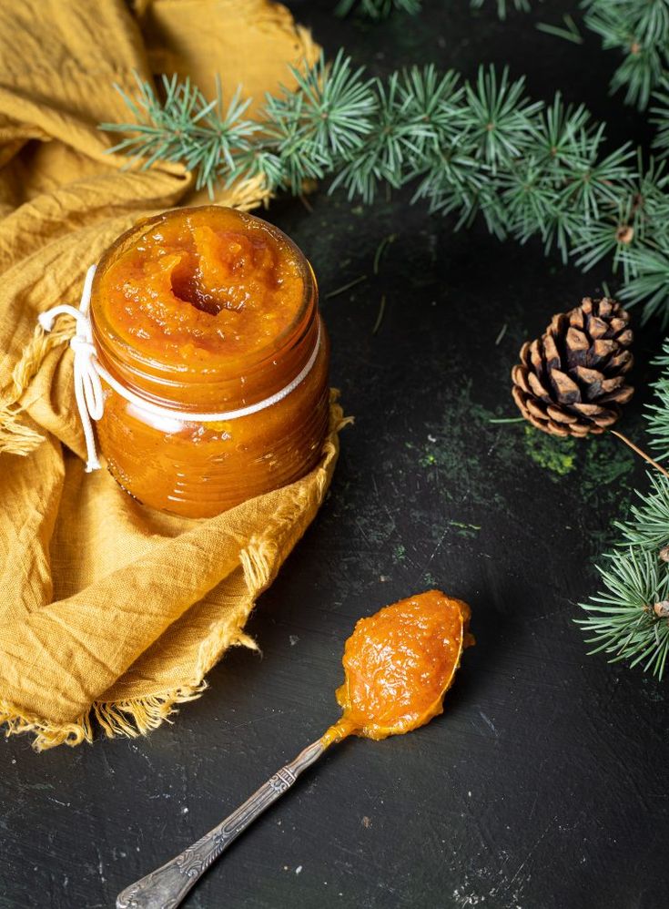 a jar of orange marmalade sitting on top of a table next to pine cones