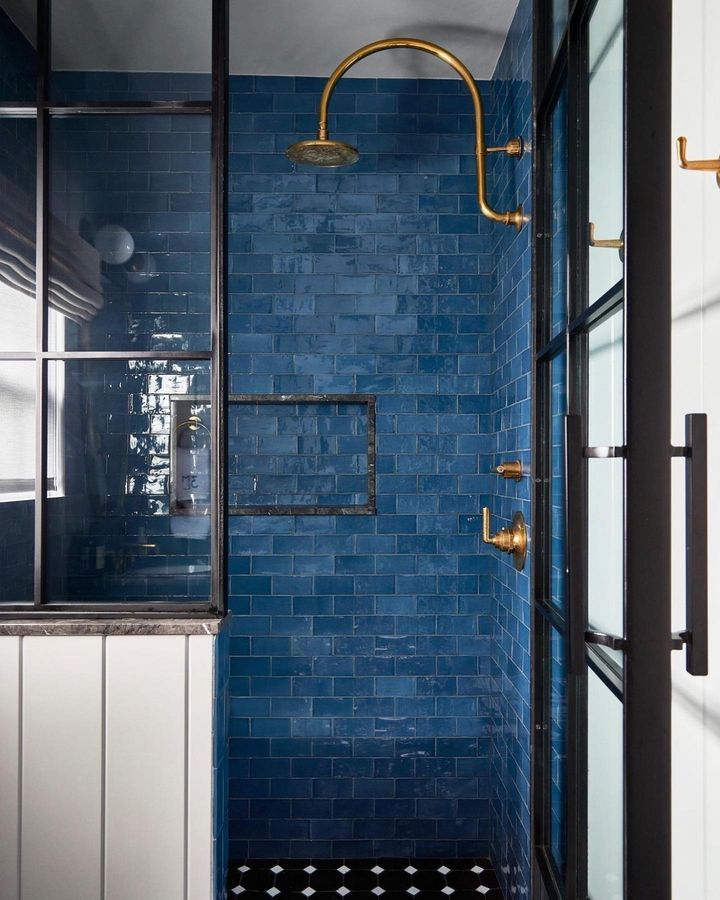 a blue tiled bathroom with black and white flooring, gold fixtures and shower head