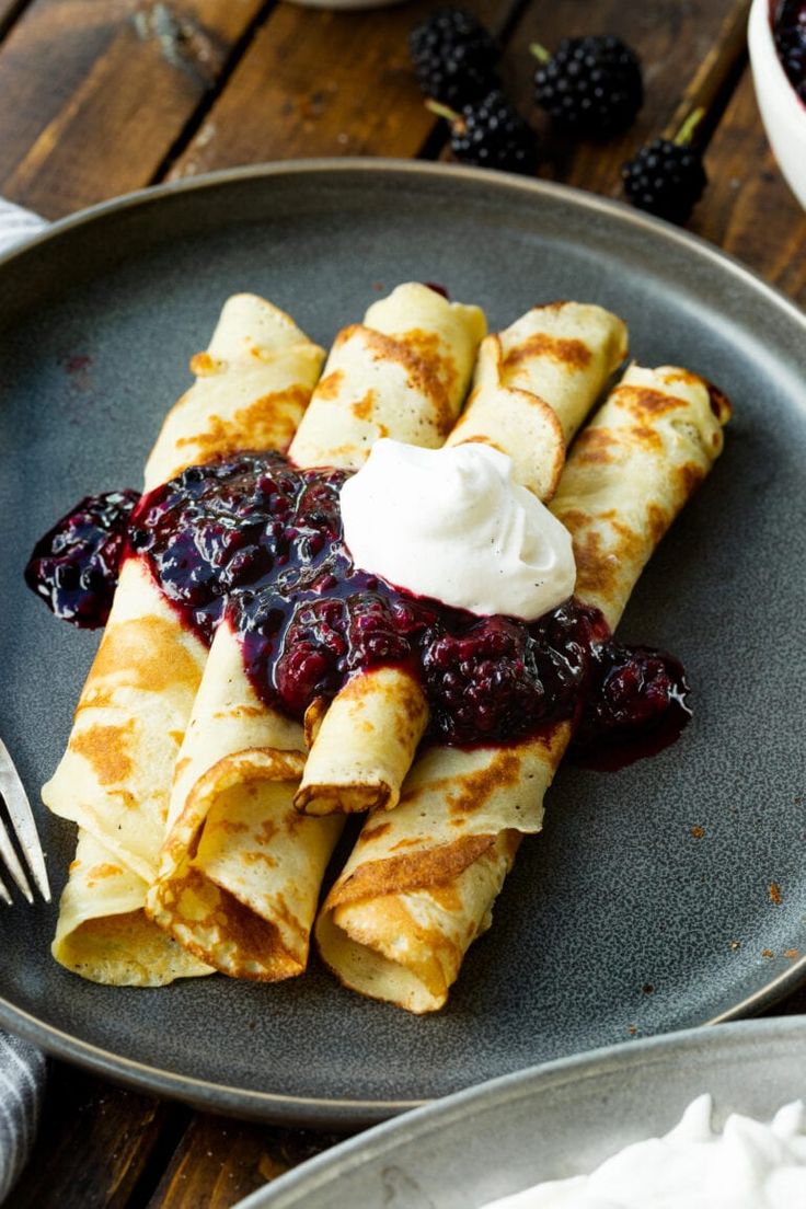 crepes with blueberry sauce and whipped cream are on a plate next to blackberries