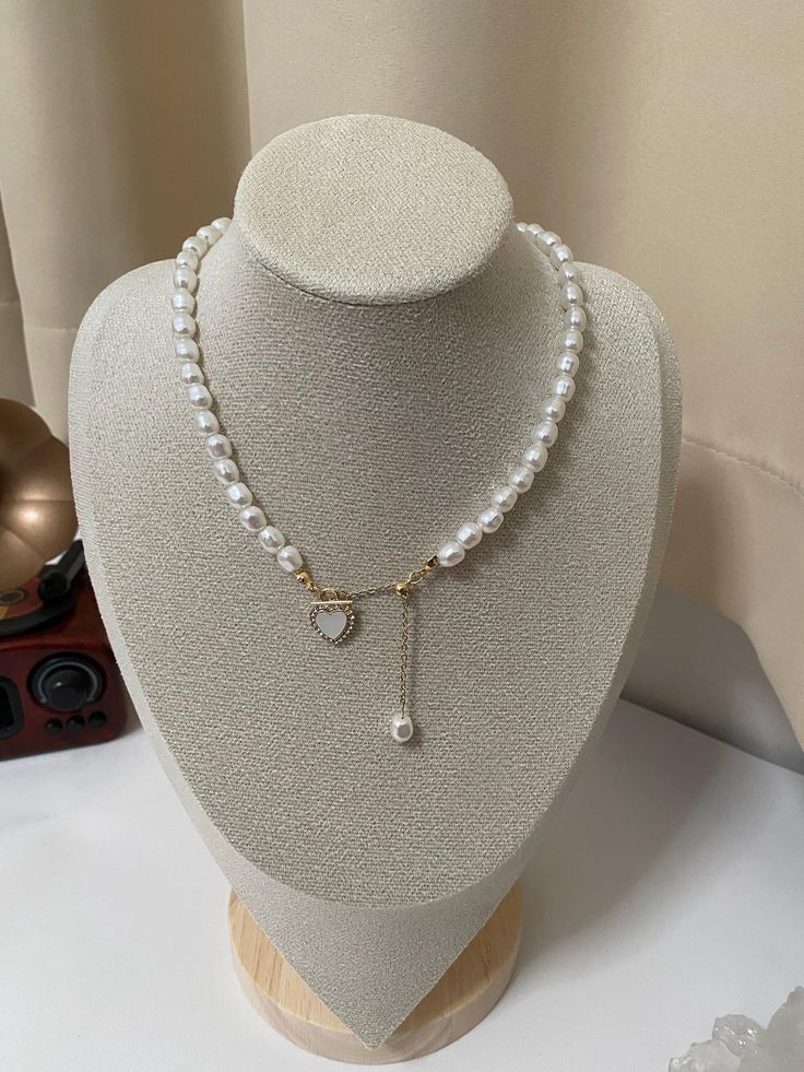 This is a classic and elegant pearl necklace, with heart-shaped pendants and hanging pearls, adding a soft and romantic temperament. The pearls are uniform and full, round and smooth, highlighting the elegant taste. The heart-shaped pendant is decorated with an exquisite golden border, which fits perfectly with the overall elegant style of the necklace. The design of the pendant adds a touch of dynism to the overall shape, which is very suitable for various formal or casual occasions, showing the wearer's delicate taste and fashion sense. White Pearl Drop Necklace For Valentine's Day, White Pearl Clavicle Chain Necklace For Valentine's Day, White Pearl Clavicle Necklace For Valentine's Day, Gold Heart-shaped Pearl Necklace, Valentine's Day Pearl Clavicle Chain Necklace, Valentine's Day White Pearl Clavicle Necklace, Valentine's Day White Pearl Necklace With Charm, Valentine's Day Gold Pearl Necklace, White Pearl Heart Pendant Necklace