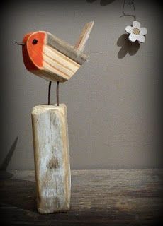 a wooden bird sitting on top of a piece of wood next to a white flower