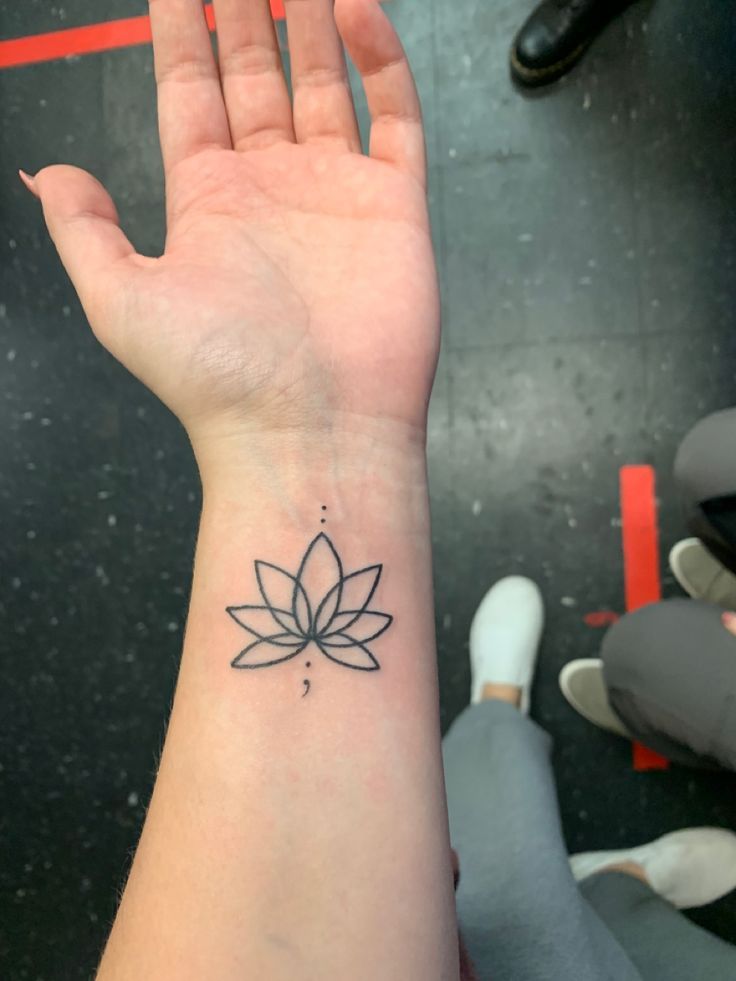 a person's hand with a small tattoo on the wrist that has a lotus flower on it